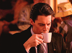 Close up gif of Agent Cooper from Twin Peaks. A smile grows on his face as he savours the first sip of his cup of coffee.