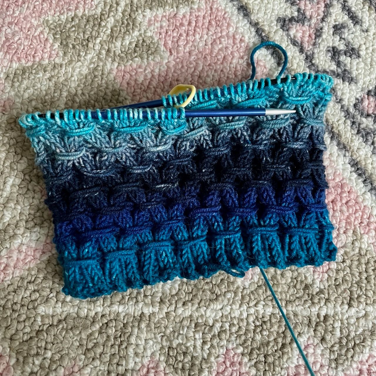 mostly knitted cowl with a diamond shaped pattern. Colors are a range of blues going from a dark turquoise to navy blue back to turquoise
